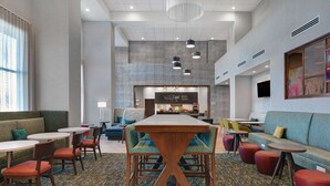 A modern lounge area with a central wooden table, multiple seating options including sofas and chairs, and a patterned carpet.