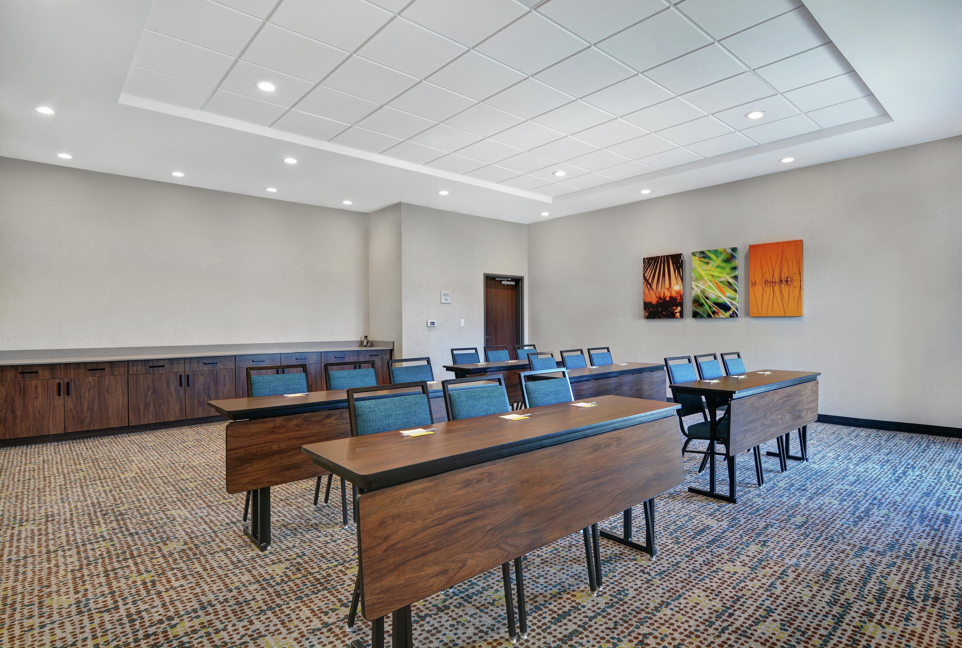 A conference room with a long table, multiple chairs, a podium, and three artworks on the wall.