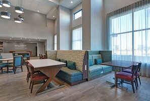 A modern hotel lobby with a reception desk, seating area, and large windows.