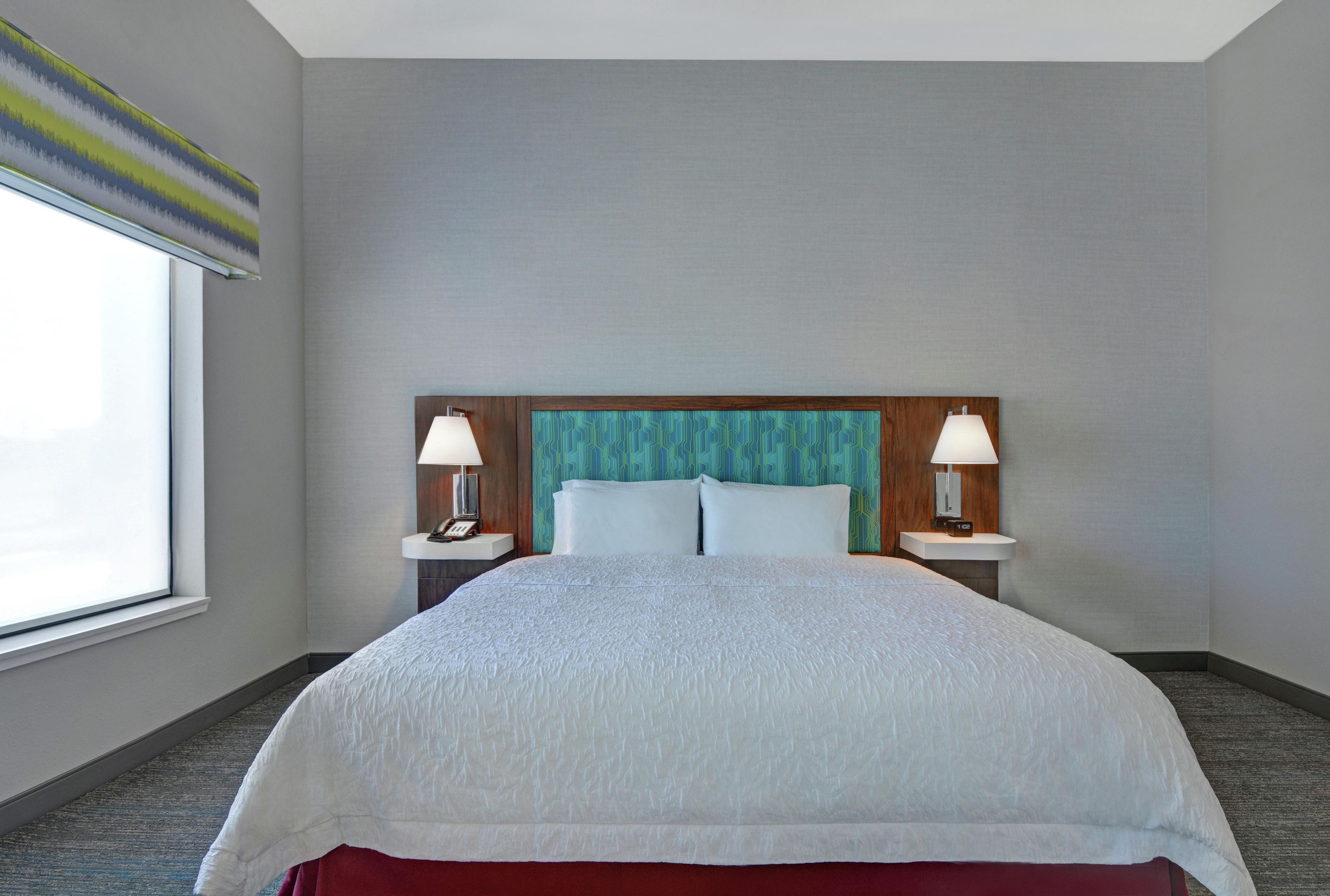 A hotel room with a large bed, two bedside lamps, a wooden headboard, and a window with a view.