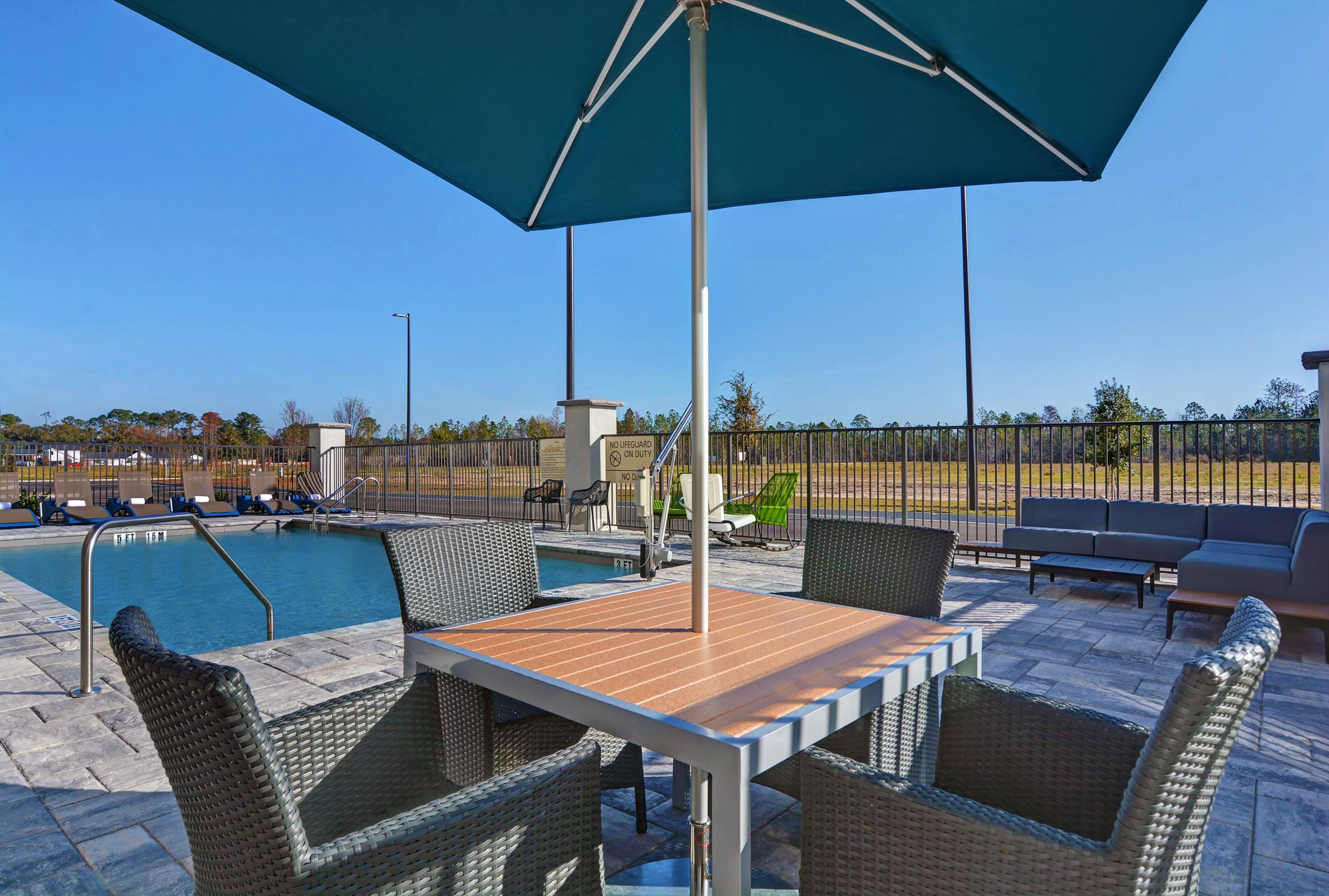 An outdoor pool area with a table and chairs, a lifeguard sign, and a fenced area.