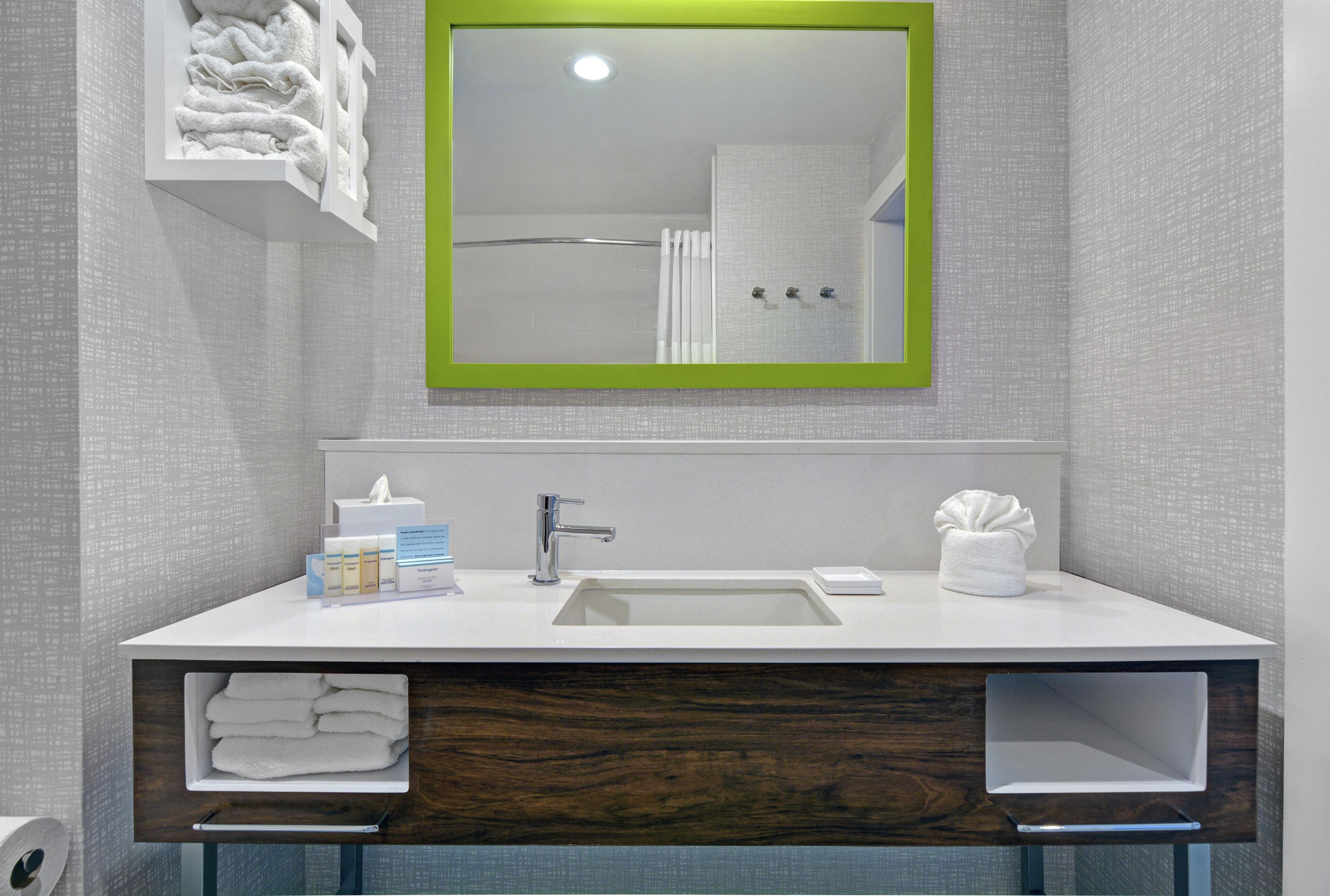 Un baño moderno con un lavabo blanco, un espejo con marco verde y toallas dobladas con cuidado.