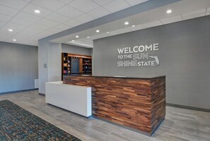 Un mostrador de recepción con un cartel que dice 'Welcome to the Sun Shinesate', un área de recepción de madera y una alfombra estampada.