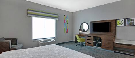 Habitación de hotel con una cama grande, un escritorio con silla, televisor y ventana con persianas.