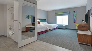 A modern hotel room with a sliding door leading to a bathroom, a large bed with a view of the city, a desk with a chair, and a window with a view of the city.