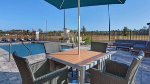 A poolside area with a table and chairs, a pool, and a fenced area with lounge chairs.