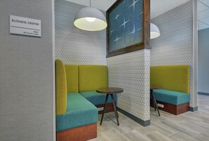 A business center with a sign indicating 24-hour operation, a seating area with green and blue upholstered benches, and a patterned wall.
