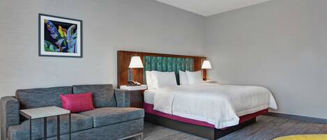 A hotel room with a bed, a gray sofa, a small table, and a chair.