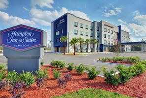 Hampton Inn & Suites by Hilton -hotellin kyltti ja moderni rakennus, jossa on useita ikkunoita ja lippu.