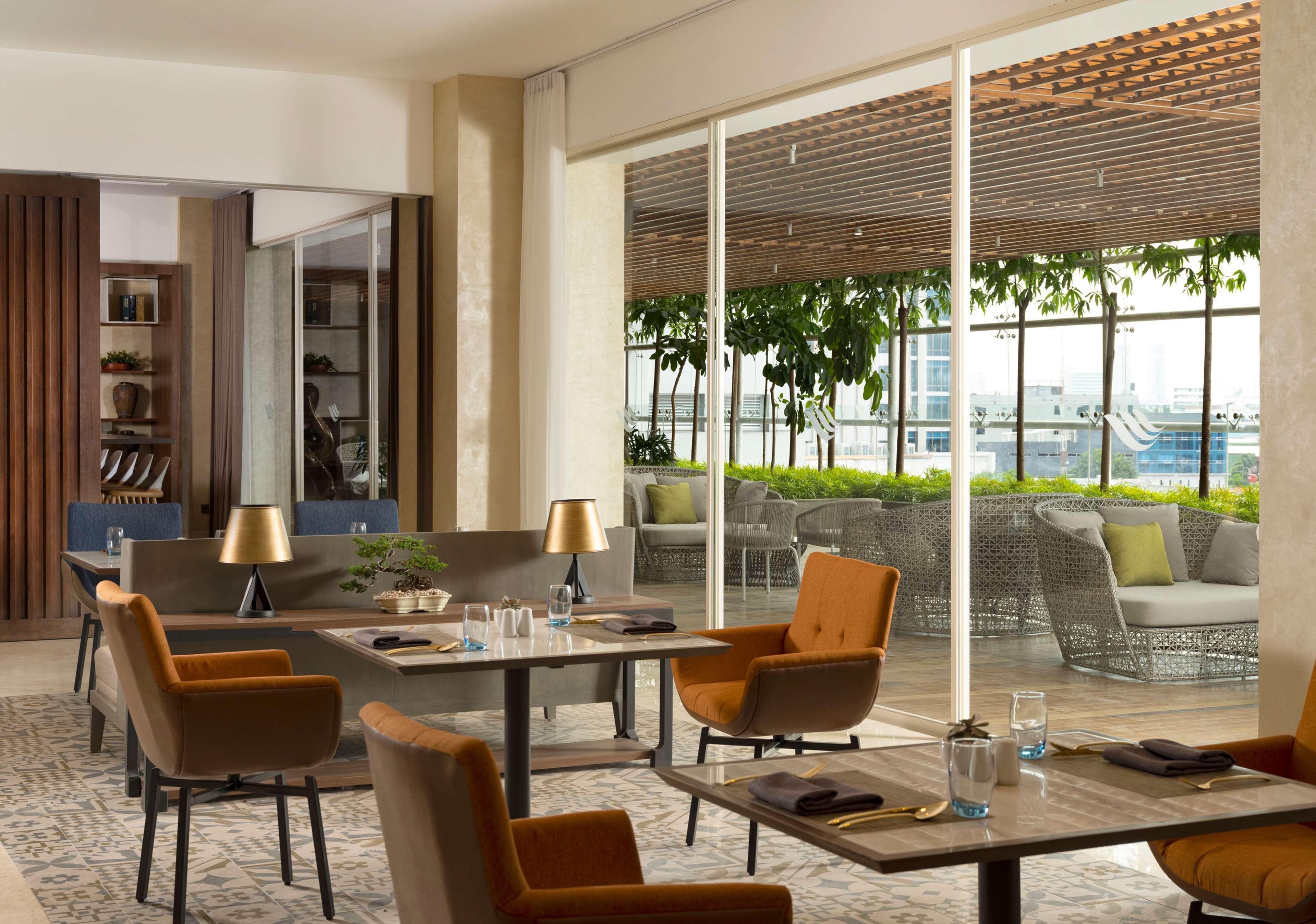 A modern hotel lobby with a dining area, seating arrangements, and a view of the cityscape through large windows.