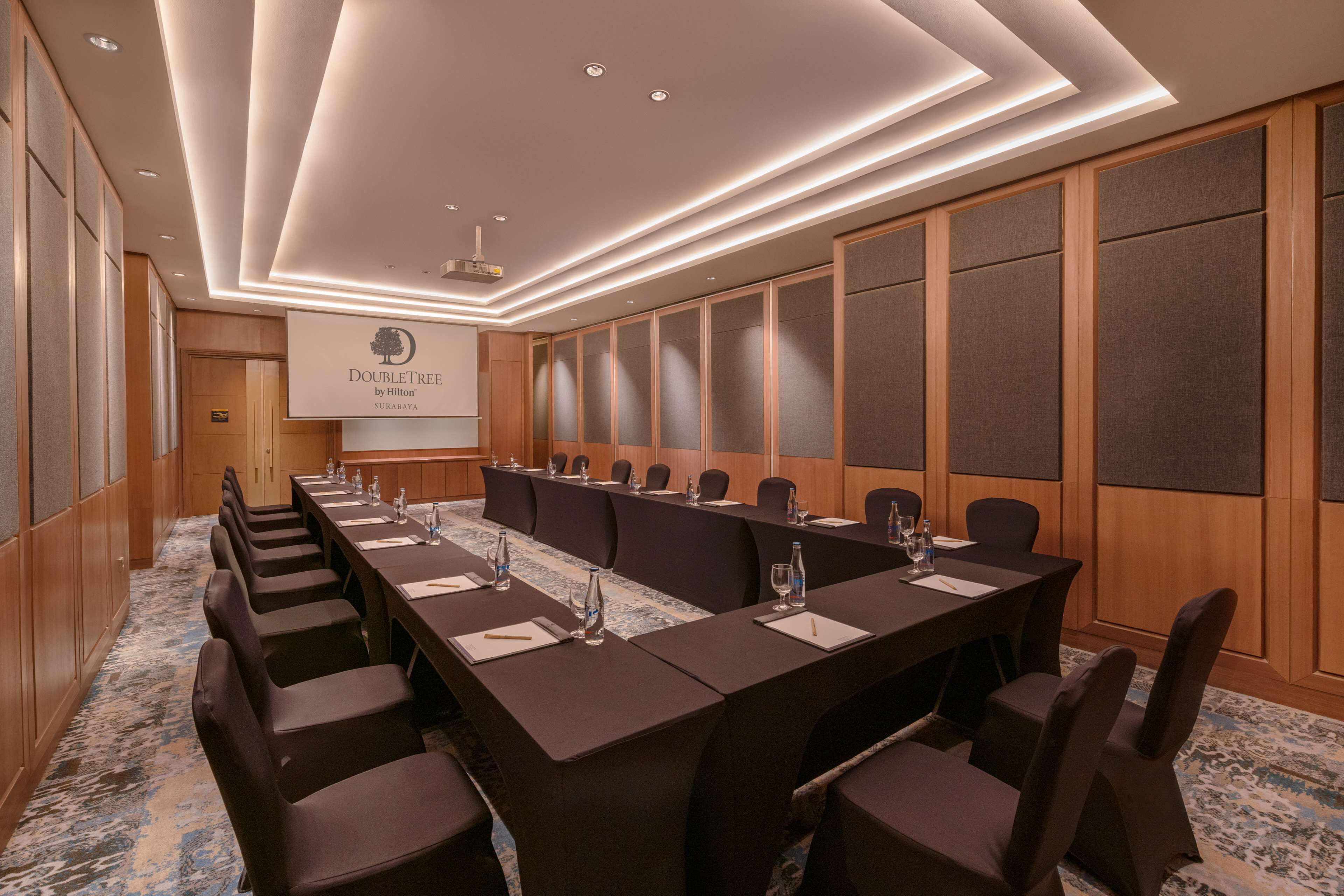 A conference room with a long table, chairs, and a projector screen displaying "DoubleTree by Hilton".
