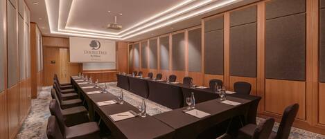 A conference room with a long table, chairs, and a projector screen displaying "DoubleTree by Hilton".