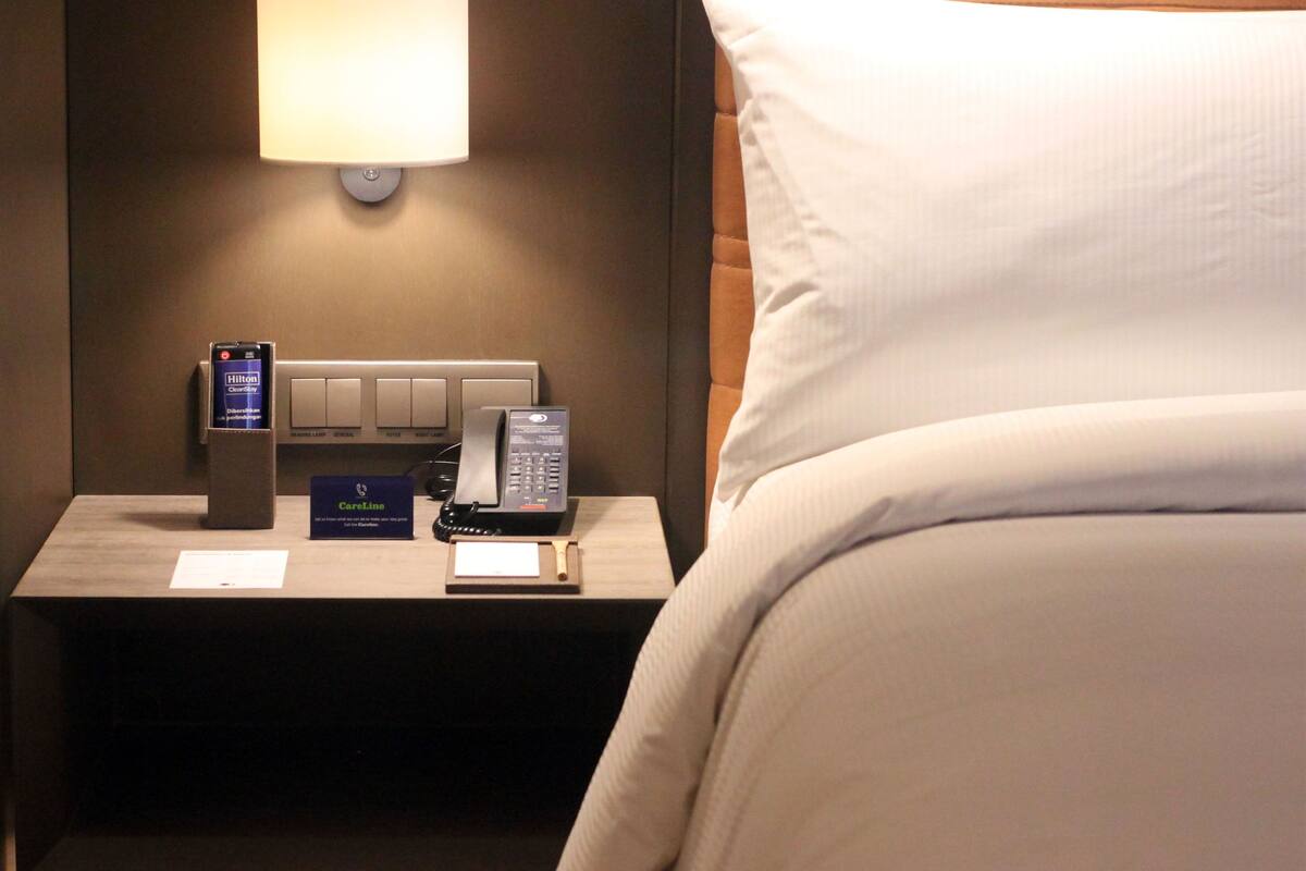 Ein Hotelzimmer mit einem Nachttisch, der ein Telefon, ein Kartenlesegerät und eine Lampe zeigt.
