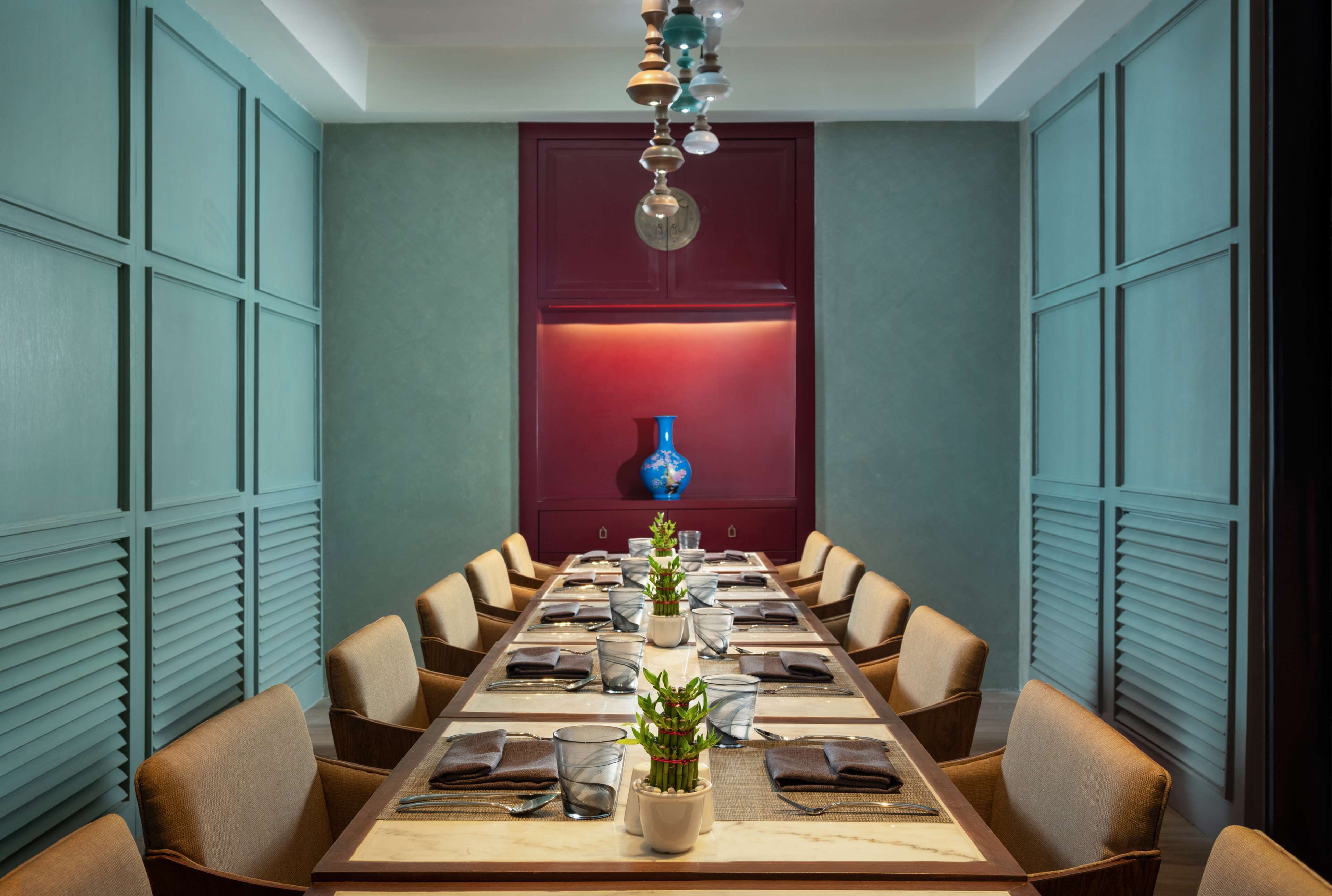 A conference room with a long table set for a meeting, surrounded by chairs, with a decorative vase on the wall behind the table.