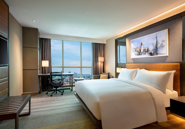 A hotel room with a large bed, a desk, a chair, a TV, and a city view. - Doubletree By Hilton Surabaya (Surabaya)
