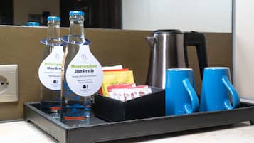 Una bandeja con botellas de agua, una cafetera y tazas azules sobre una encimera de hotel.