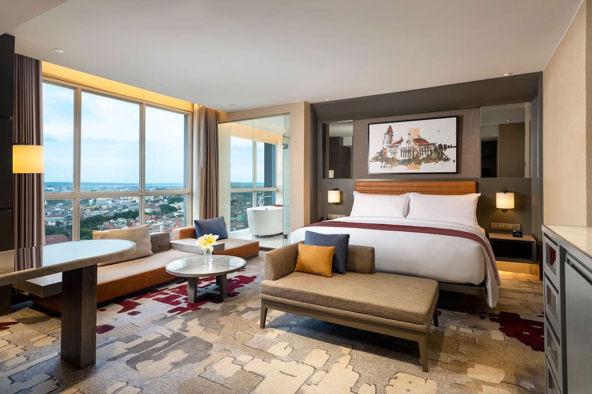 Ein modernes Hotelzimmer mit einem großen Bett, einer Couch, einem kleinen Tisch und Blick auf die Stadt.