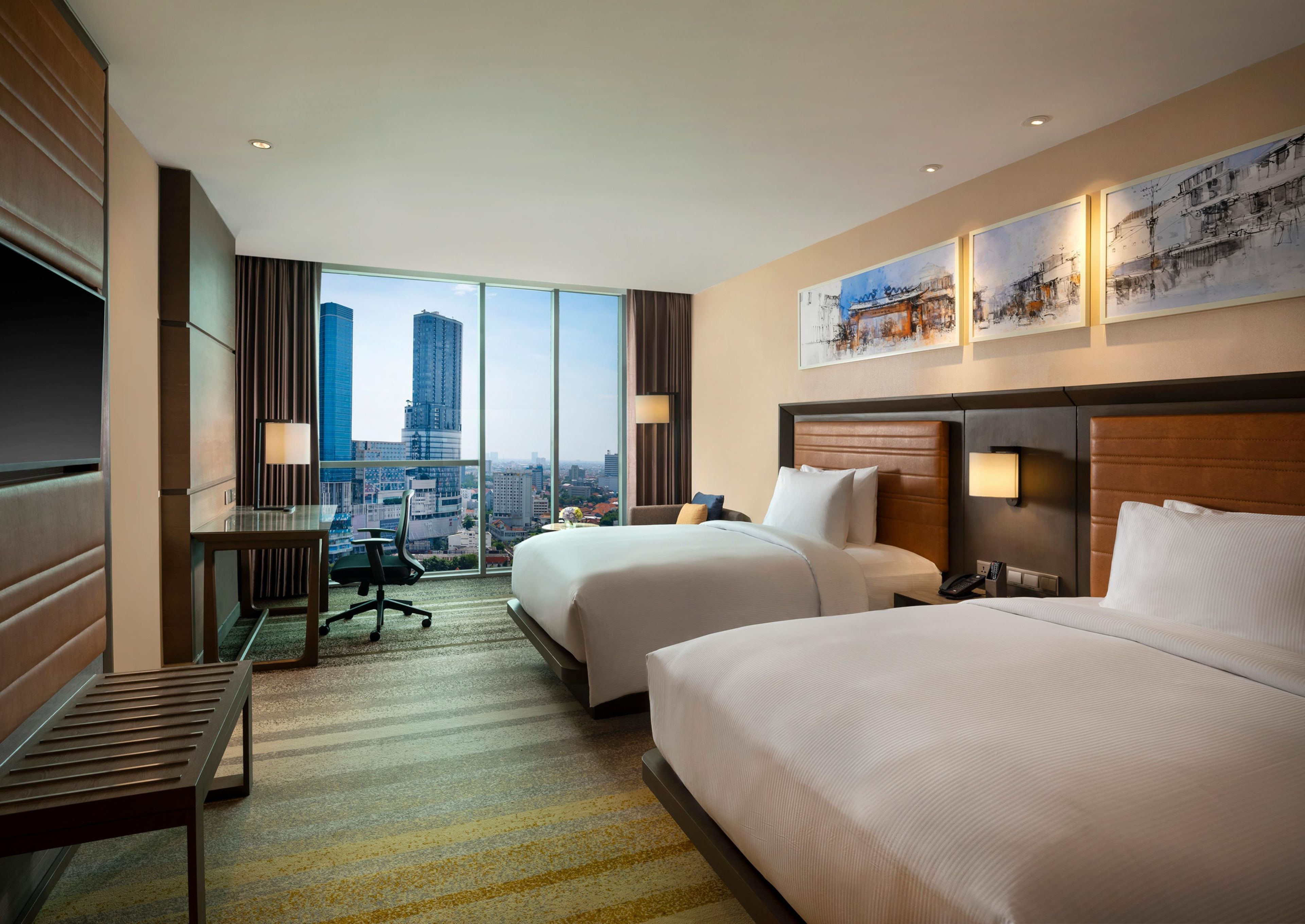 Une chambre d’hôtel avec deux lits, un bureau et une grande fenêtre donnant sur la ville.