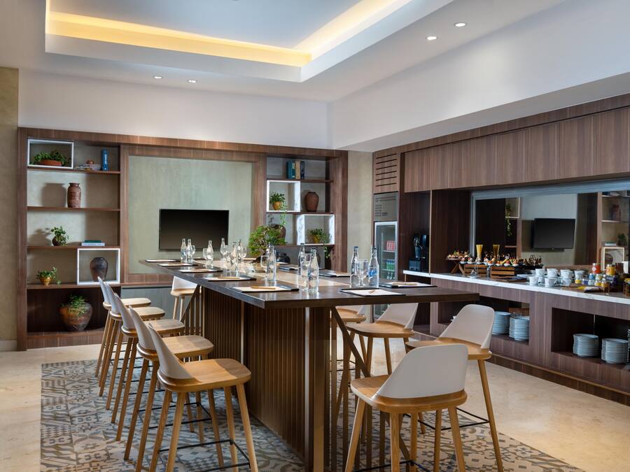 Una cocina moderna con una isla central, taburetes de bar y estanterías empotradas decoradas con objetos ornamentales.