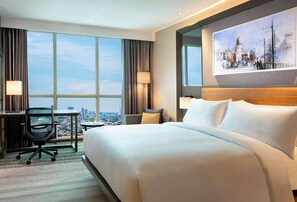 A hotel room with a large bed, a desk, a chair, and a city view through large windows. - Doubletree By Hilton Surabaya (Surabaya)