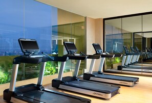 Eine Reihe von Laufbändern mit digitalen Bildschirmen in einem modernen Fitnessstudio mit großen Fenstern und Blick auf die Stadt.