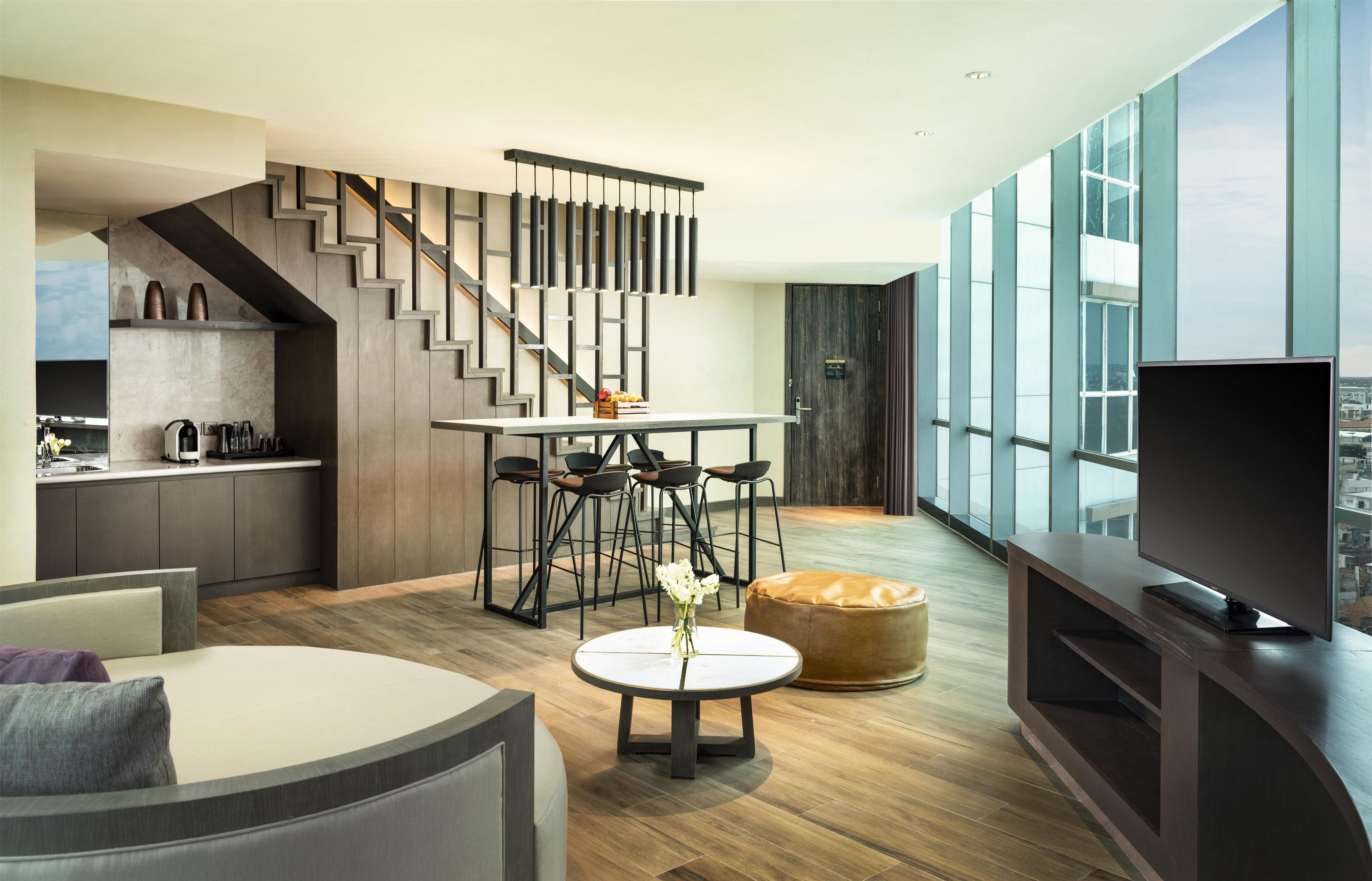 A modern living space with a kitchen, dining area, and a large window overlooking a cityscape.