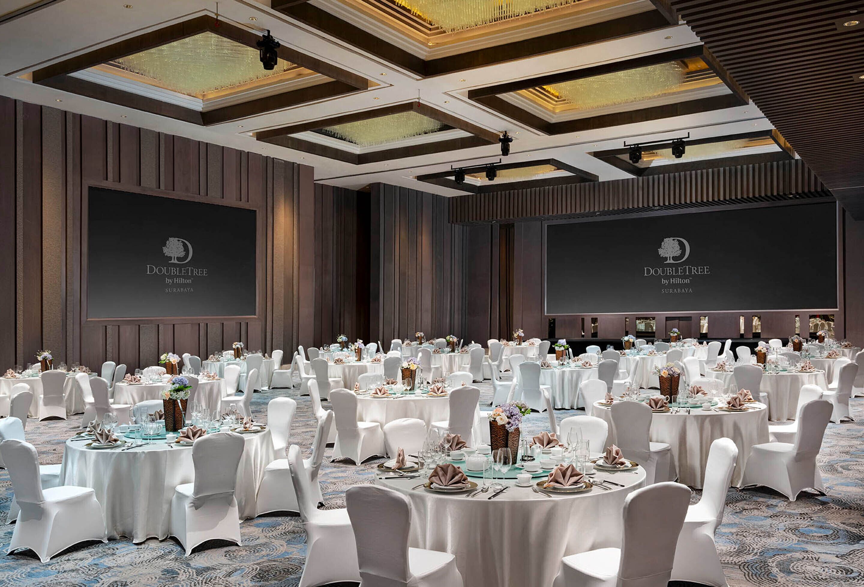 Un amplio salón de banquetes con mesas redondas dispuestas para un evento formal, con sillas blancas y vajilla elegante.