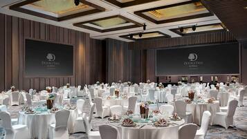 Un amplio salón de banquetes con mesas redondas dispuestas para un evento formal, con sillas blancas y vajilla elegante.