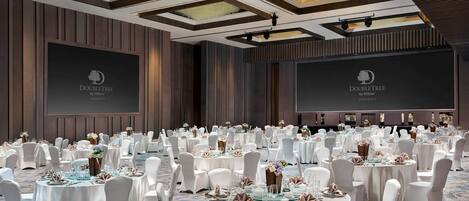 Un amplio salón de banquetes con mesas redondas dispuestas para un evento formal, con sillas blancas y vajilla elegante.
