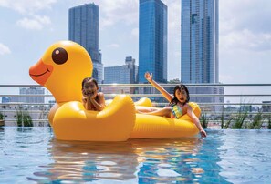 Una piscina con dos niños sobre un pato gigante inflable.