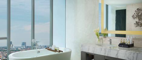 Un baño moderno con una bañera grande, un tocador de mármol y vistas a la ciudad a través de amplias ventanas.
