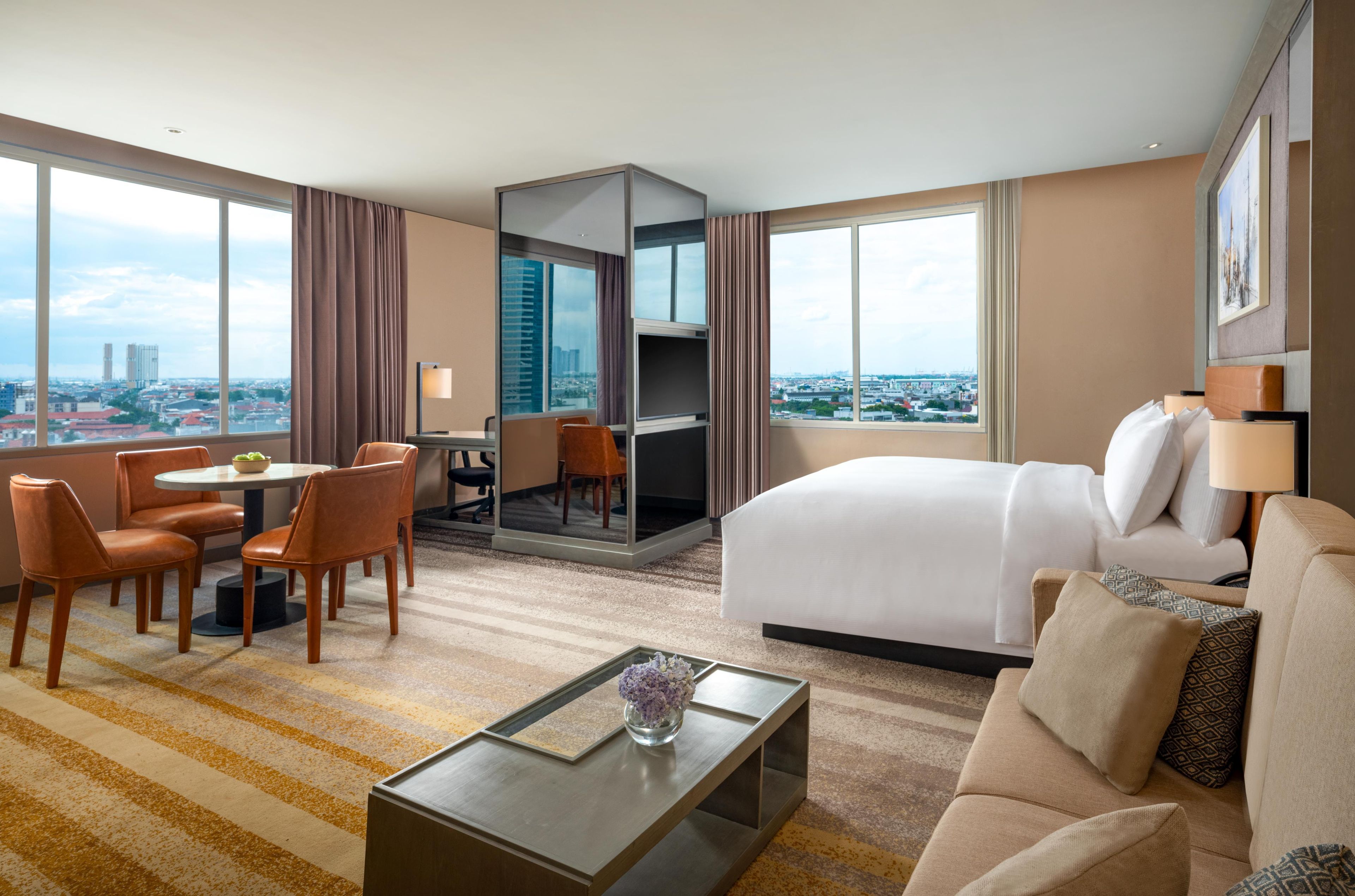 Ein Hotelzimmer mit Bett, Sofa, Couchtisch, Schreibtisch mit Stuhl und Blick auf die Stadt.