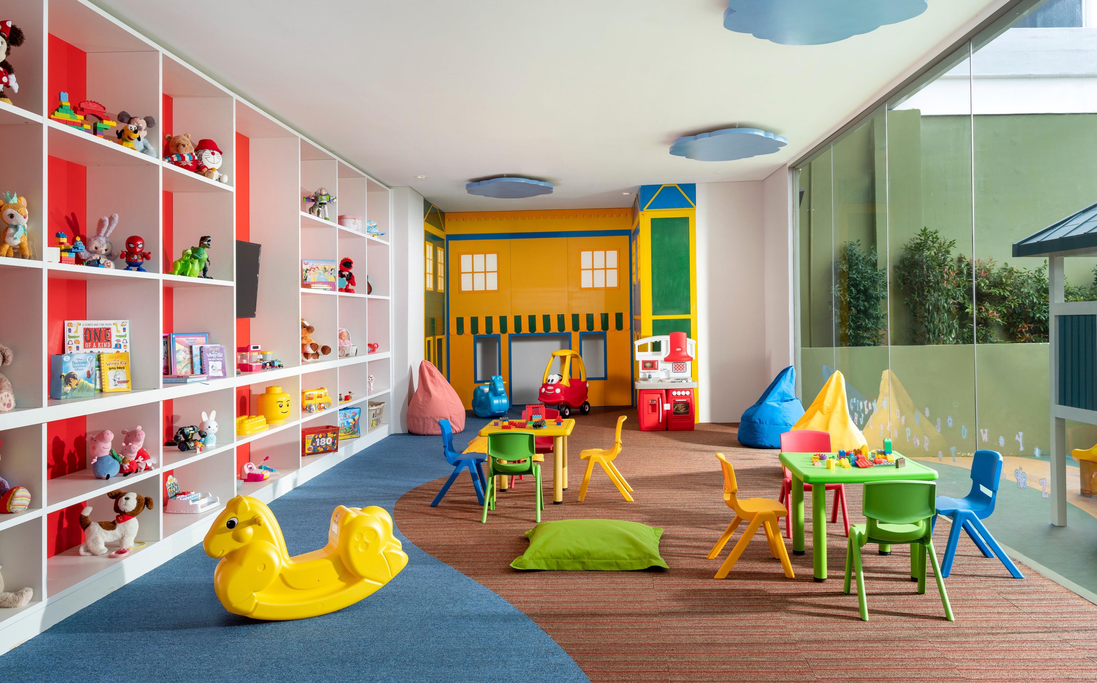 Una sala de juegos infantiles con alfombra azul, juguetes coloridos y un ventanal grande.