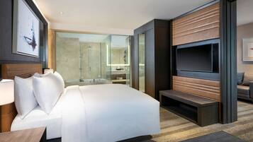 Una habitación de hotel moderna con una cama grande, un televisor, una zona de estar y ducha con mampara de vidrio.