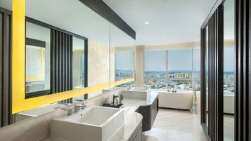 A modern bathroom with two sinks, a large mirror, and a view of the city.