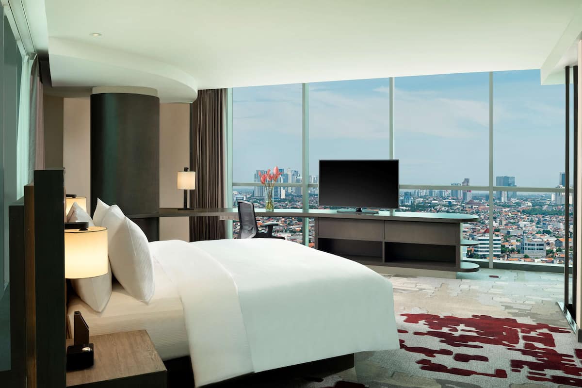 Ein modernes Hotelzimmer mit einem großen Bett, einem Flachbildfernseher, einem Schreibtisch und Blick auf die Stadt.