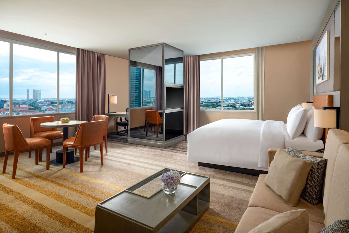 Ein Hotelzimmer mit Bett, Sofa, Essbereich mit Stühlen, Fernseher und Blick auf die Stadt.