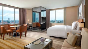 A hotel room with a bed, a sofa, a dining area with chairs, a TV, and a city view.
