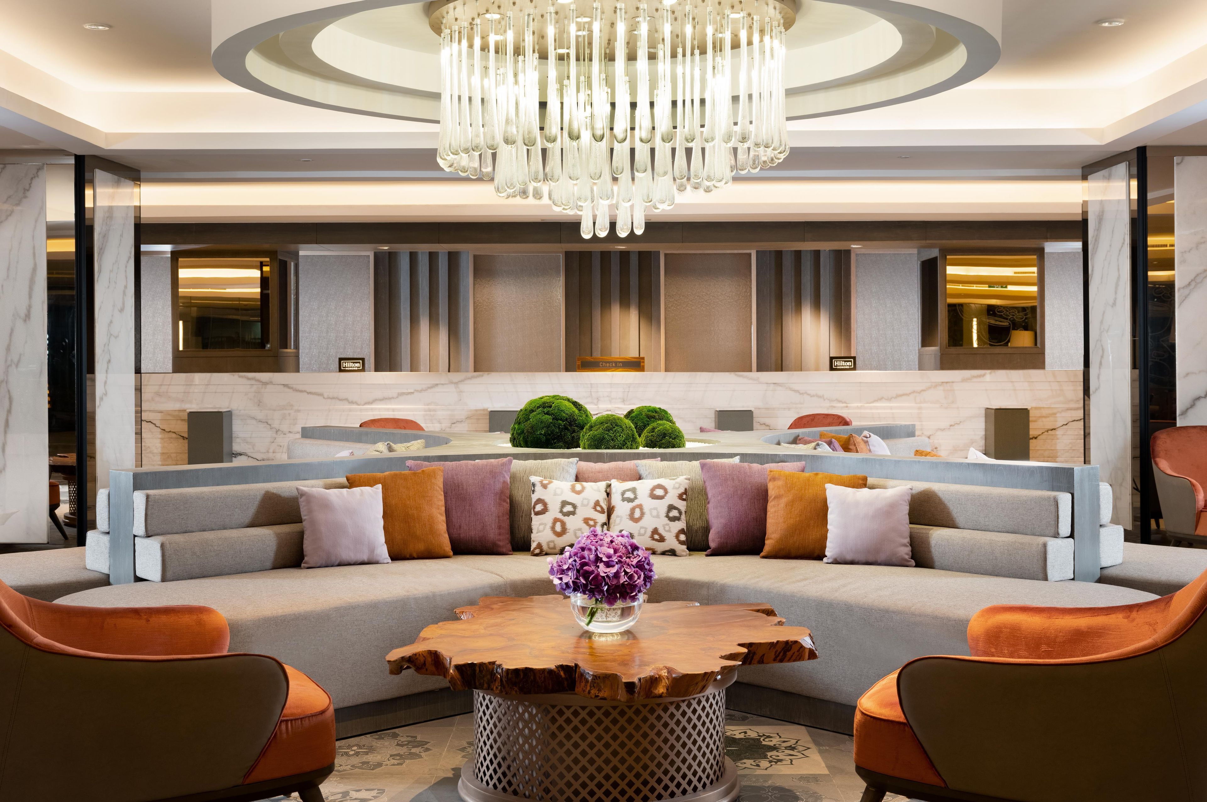 A modern hotel lobby with a large seating area, a wooden coffee table, and a chandelier.