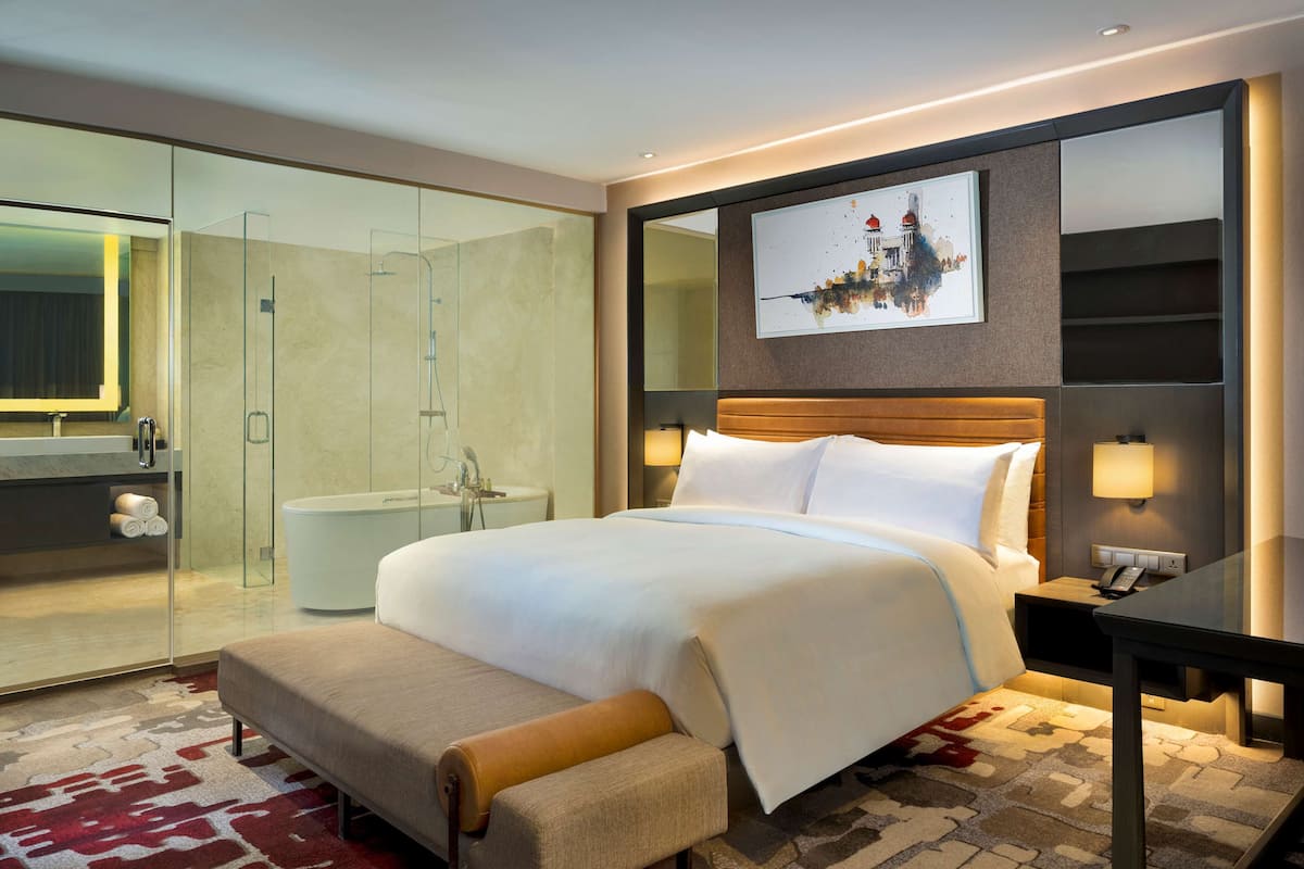 Ein modernes Hotelzimmer mit einem großen Bett, einer Dusche mit Glastrennwand, einem Nachttisch mit Lampe und einem Wandbild.