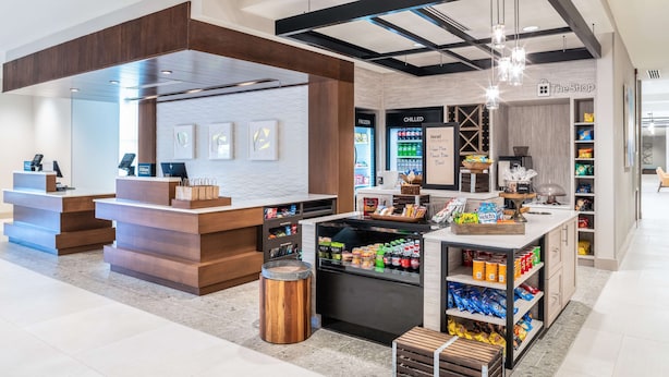 Un espacio comercial moderno con mostrador de recepción, dispensadores de bebidas frías y estantes llenos de aperitivos y bebidas.
