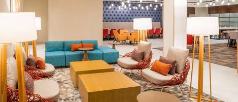 En moderne lobby med en blå sofa, orange og røde stole, træborde og en væg med mønster.