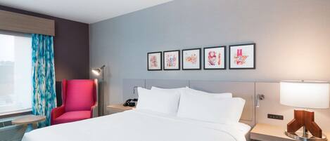 A hotel room with a large bed, a red armchair, a bedside table with a lamp, and a window with curtains.