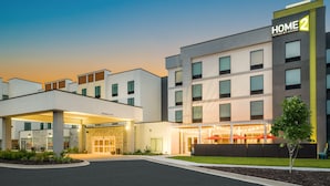 Un hotel moderno con una entrada bien iluminada, varios pisos y un letrero claro que dice 'HOME 2 Suites by Hilton'.