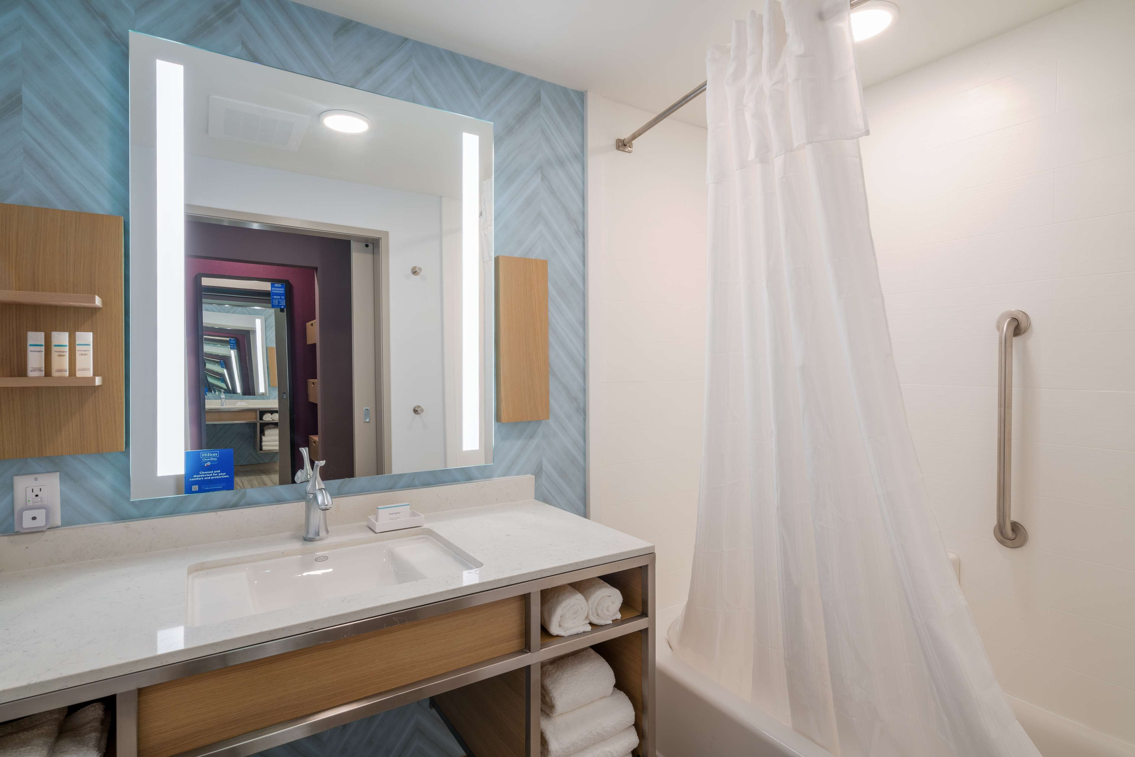Un baño moderno con un espejo grande, lavamanos blanco y una ducha con cortina.