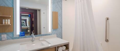 A modern bathroom with a large mirror, white sink, and a shower with a curtain.