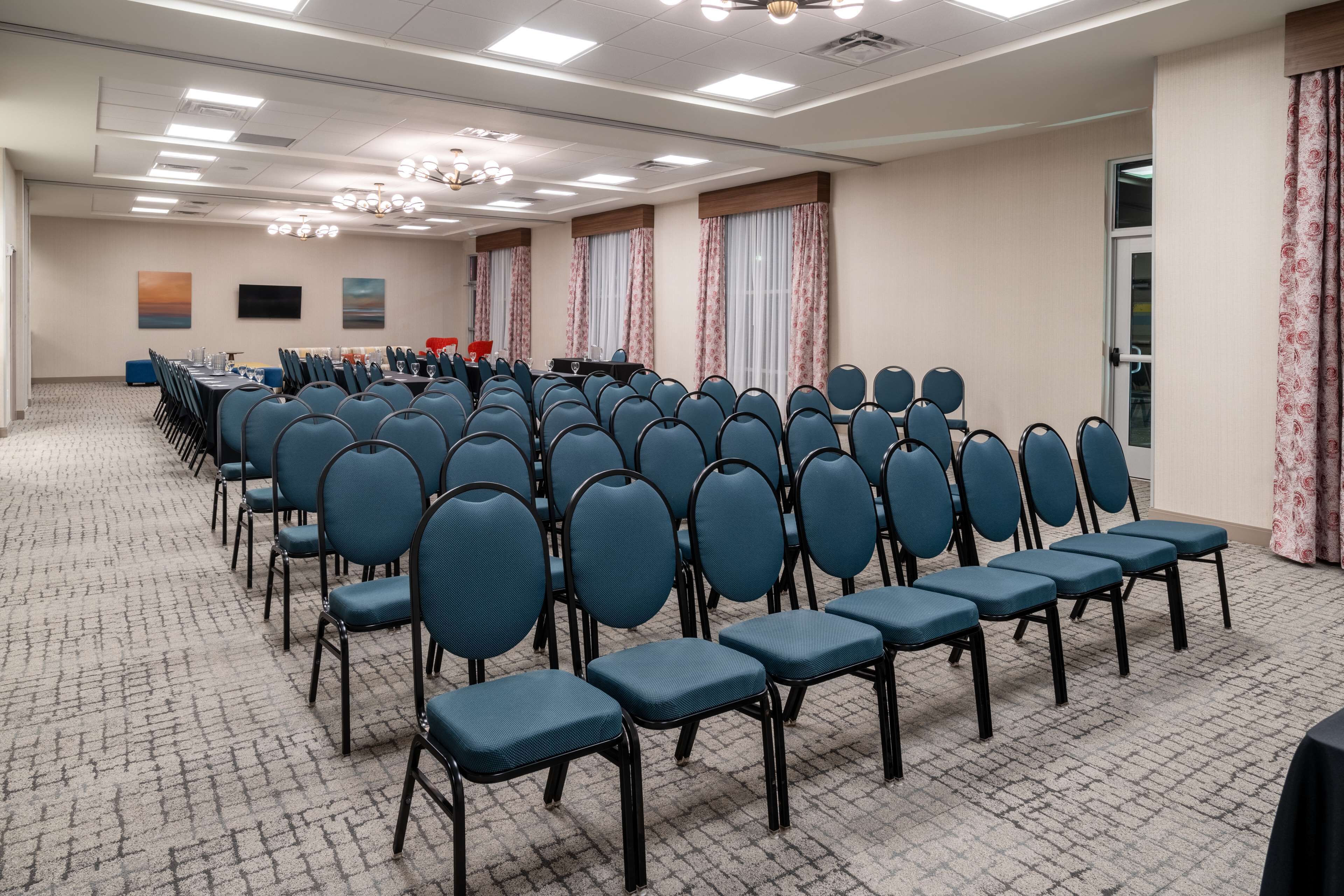 A conference room with rows of blue chairs, a long table, and a chandelier.