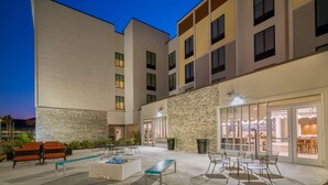 Un patio de hotel moderno con mobiliario exterior, una piscina y un restaurante.