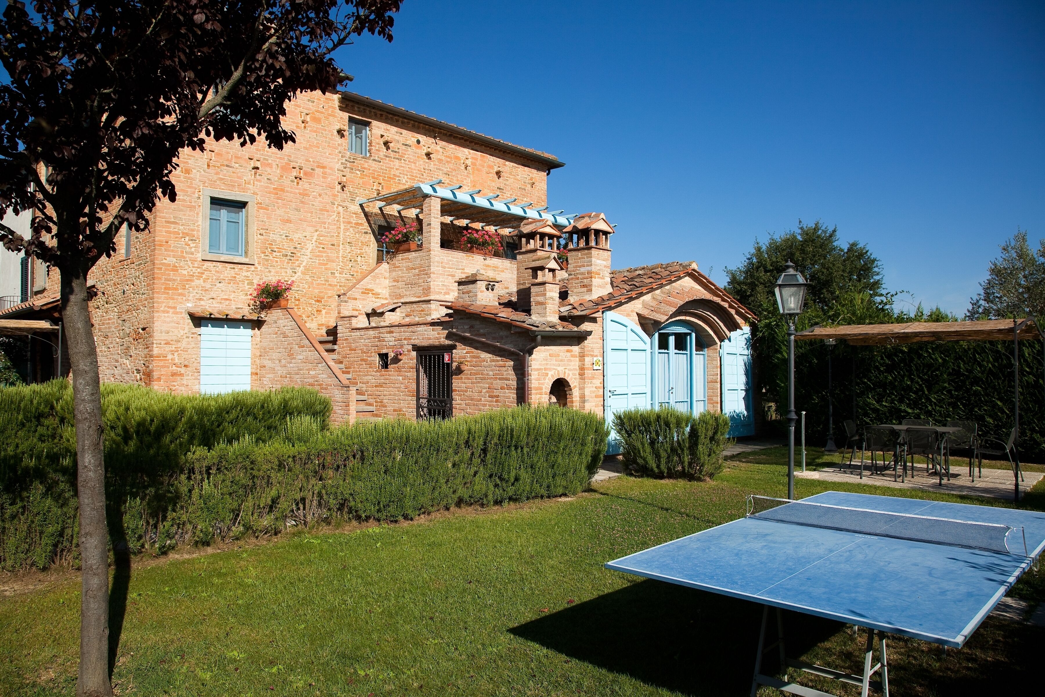Un bâtiment traditionnel en briques avec une porte bleue, un court de tennis et un jardin bien entretenu.