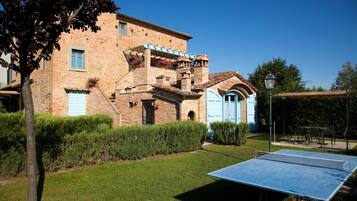 Un bâtiment traditionnel en briques avec une porte bleue, un court de tennis et un jardin bien entretenu.